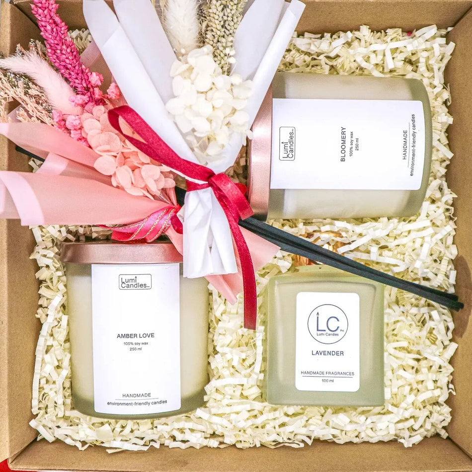 Wellness Ensemble Gift Set opened in its kraft box, showing two LUMI Scented Soy Candles, a LUMI Reed Diffuser, and two dried flower bouquets tied with a pink ribbon