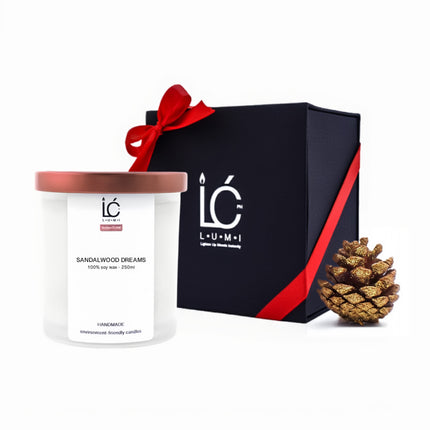 Sandalwood Dreams LUMI Scented Soy Candle (250ml) in a frosted glass jar with rose gold lid, styled beside its gray gift box with ribbon and gold pine cone for bulk holiday gifting.
