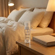 Lavender LUMI Room and Linen Spray (100ml) bottle styled on a nightstand in a cozy, lamp-lit evening scene with a book