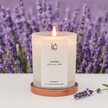 Lit Lavender scented soy candle in a frosted glass jar with rose gold base, set against a blurred lavender field with a lavender sprig in the foreground