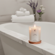 Lit Lavender Scented Soy Candle placed on a marble bathtub ledge with rolled white towels and lavender flowers, spa-style relaxation scene