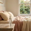 Secret Garden LUMI Room and Linen Spray (100ml) bottle styled on a nightstand in a pink and cream-linen daylight bedroom scene
