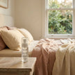 Secret Garden LUMI Room and Linen Spray (50ml) bottle styled on a nightstand in a pink and cream-linen daylight bedroom scene